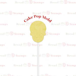 May include: A yellow cake pop mold shaped like a skull. The mold is on a white stick and the text "Cake Pop Mold" is written in red above the mold.