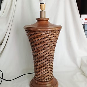 May include: A brown wicker table lamp with a wooden base and top. The lamp has a woven basket-like design and a standard light bulb socket. The lamp is approximately 71 cm tall.