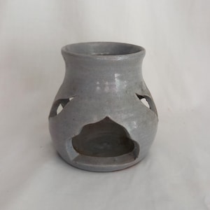 May include: A gray ceramic vase with cut-out designs. The vase has a rounded body and a flared rim. The cut-outs are in a decorative pattern. The vase is unglazed and has a matte finish.