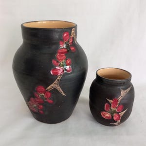 May include: Two black ceramic vases with red floral designs. The larger vase is taller and wider than the smaller vase.
