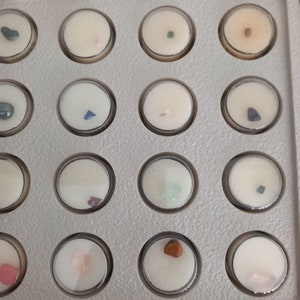 Puede incluir: Una colecci&oacute;n de peque&ntilde;as piedras preciosas de colores exhibidas en una bandeja gris con compartimentos circulares transparentes. Cada gema est&aacute; colocada sobre una base de espuma blanca. Las piedras preciosas var&iacute;an en color, incluyendo azul, rosa, verde y marr&oacute;n.