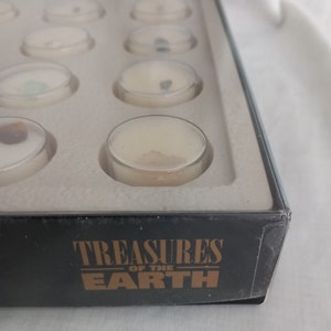Puede incluir: Una caja negra con la inscripci&oacute;n dorada "Treasures of the Earth", que contiene peque&ntilde;os recipientes con tapa transparente. Cada recipiente contiene una muestra de tesoros de la tierra. Los recipientes est&aacute;n dispuestos en filas dentro de un inserto blanco.