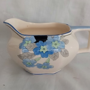 May include: A white ceramic jug with a blue and grey floral design. The jug has a rounded body and a handle.