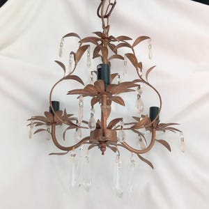 May include: A bronze chandelier with a floral design and hanging crystal accents. The light fitting has three light sockets and is suspended from a chain. The chandelier's design includes leaf-shaped elements.