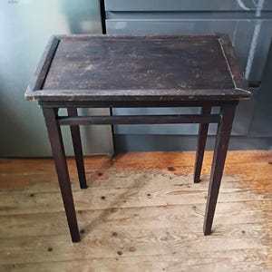 May include: A small, dark brown wooden side table with a rectangular top and four slender legs. The table has a simple, classic design, and the wood grain is visible. The table is approximately 61 cm tall.