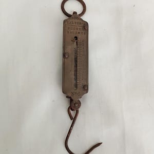 Peut inclure: Une balance de poche en laiton de marque Salter's, dotée d'un anneau de suspension supérieur et d'un crochet inférieur. Le corps métallique rectangulaire porte l'inscription Salter's Pocket Balance et No 6, avec une échelle graduée de 0 à 25.