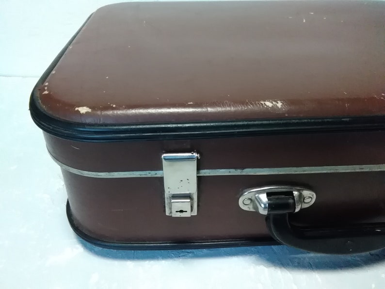 Może przedstawiać: Brązowa vintage'owa walizka z srebrnym zamkiem i czarnym uchwytem. Walizka ma zużyte sk&oacute;rzane wykończenie i czarną obw&oacute;dkę wok&oacute;ł krawędzi.