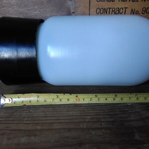 May include: A cylindrical, off-white glass lamp shade with a black rim. The shade is approximately 8 inches long. The lamp shade is on a wooden surface.