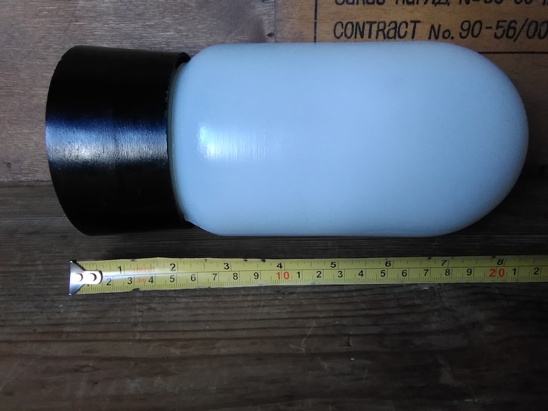 May include: A cylindrical, off-white glass lamp shade with a black rim. The shade is approximately 8 inches long. The lamp shade is on a wooden surface.