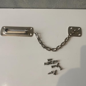 May include: A silver-toned metal door security chain guard featuring a rectangular mounting plate with a sliding track and a smaller square mounting plate connected by a linked chain. Seven small silver-coloured metal screws are included below.