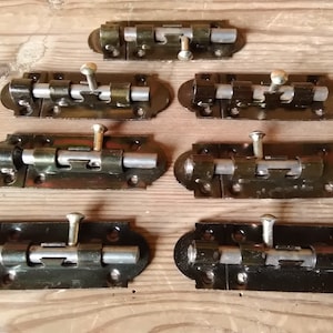 May include: Seven black metal door bolt latches with silver metal handles and a silver metal rod. The latches are arranged in two rows of three and one row of one.