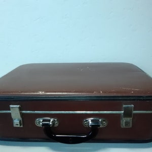 Może przedstawiać: Brązowa vintage walizka z metalowymi klamrami i czarnym uchwytem.