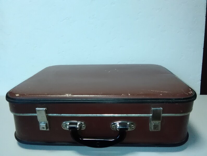 Może przedstawiać: Brązowa vintage walizka z metalowymi klamrami i czarnym uchwytem.