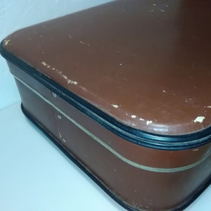 Może przedstawiać: Brązowa vintage'owa walizka z czarną obw&oacute;dką i srebrnym zamkiem. Walizka nosi ślady zużycia, co świadczy o jej wieku.