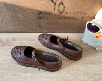 May include: Two pairs of brown leather shoes with cutouts and a buckle strap. The shoes have a rounded toe and a low heel.