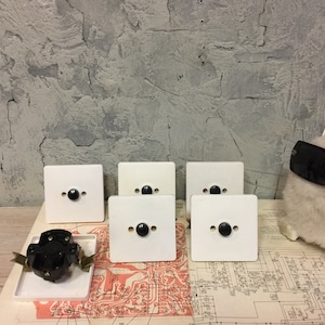 May include: Six white light switch plates with black buttons. The plates are arranged in two rows of three. The plates are on a wooden surface with a circuit diagram underneath.