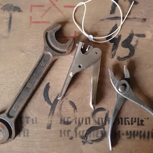 Op de afbeelding: Een set van drie gereedschappen op een houten oppervlak. De gereedschappen omvatten een moersleutel, een metalen gereedschap met een handvat en een tang.