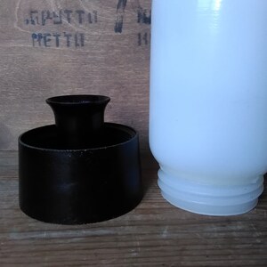 May include: A black, cylindrical object with a flared top and a white, opaque bottle. The bottle has a rounded shape and a ridged base. The objects are on a wooden surface.