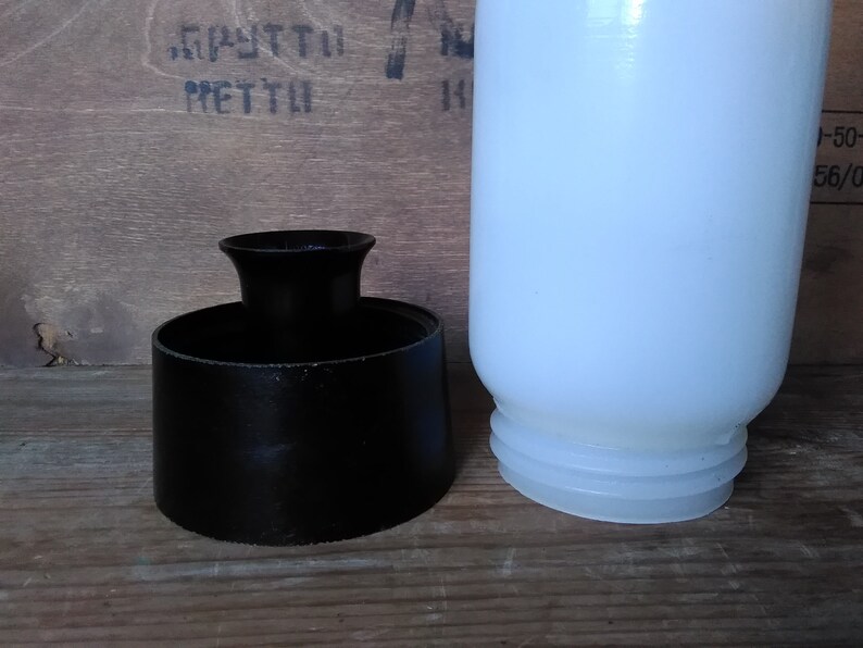 May include: A black, cylindrical object with a flared top and a white, opaque bottle. The bottle has a rounded shape and a ridged base. The objects are on a wooden surface.