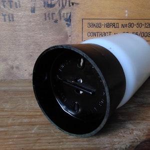 May include: A black and white cylindrical object with a rounded top. The object has a black base and a white, rounded top. The object is lying on a wooden surface. The background includes text on a wooden surface.