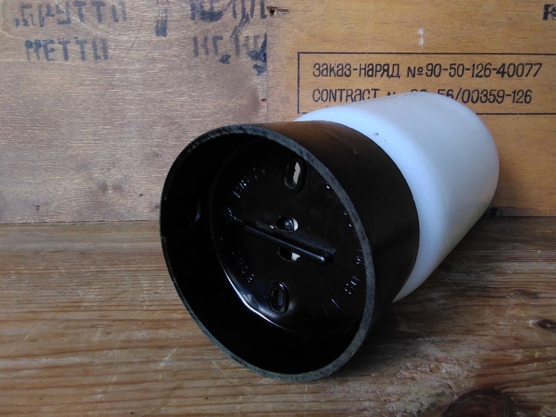 May include: A black and white cylindrical object with a rounded top. The object has a black base and a white, rounded top. The object is lying on a wooden surface. The background includes text on a wooden surface.