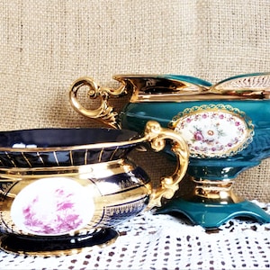 May include: Two decorative ceramic bowls with gold trim and floral designs. The larger bowl is teal green with gold accents and a floral pattern. The smaller bowl is black with gold accents and a pink floral design.