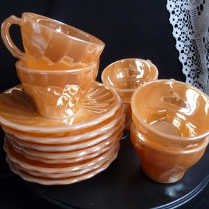 Peut inclure: Un ensemble de tasses et de soucoupes vintage de couleur orange. L'ensemble comprend plusieurs tasses avec des anses, empilées les unes sur les autres, et des soucoupes assorties. Les tasses et les soucoupes ont un design côtelé. L'ensemble est présenté sur une surface sombre.