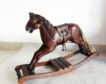 May include: A wooden rocking horse with a brown finish and a leather saddle. The horse has a long, flowing mane and tail.