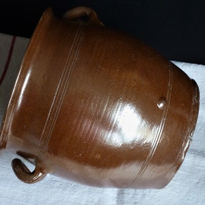 Op de afbeelding: Een grote, bruine aardewerken pot met twee handvatten. De pot heeft een glad, geglazuurd oppervlak en is versierd met drie horizontale lijnen.