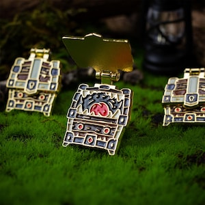 May include: Three gold-colored treasure chest pins. One chest is open and reveals a red-eyed monster with sharp teeth. The other two chests are closed.