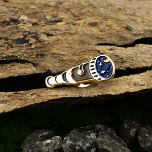 May include: Gold-toned telescope pin with a blue and white enamel design of a night sky with stars and a crescent moon.