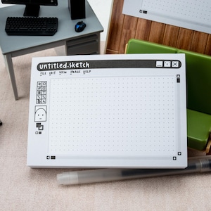 May include: A white notepad with a dotted grid, resembling a digital sketch interface. The notepad features the text "untitled.sketch" and a series of black icons. A pen rests nearby, suggesting a creative or design theme.