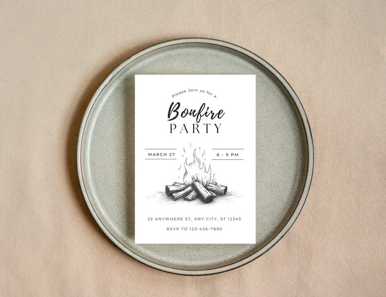 May include: A white invitation card with the words "Bonfire PARTY" in a stylish font, featuring a bonfire illustration. The card includes the date, time, and RSVP information. The invitation is placed on a gray plate.