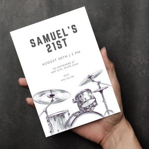 May include: A white invitation card with the text "SAMUEL'S 21ST" and event details. A black and white illustration of a drum kit is at the bottom. The card is held in a hand.