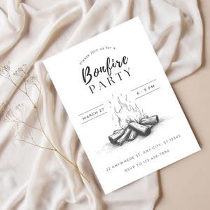 May include: A white invitation card with the text "Bonfire Party" in a script font, featuring a bonfire illustration. The card includes event details like the date, time, and RSVP information. The background is a beige surface with a white fabric.