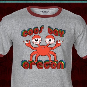 May include: A gray t-shirt with a red ringer. The shirt features a cartoon crab with red eyes and a rainbow graphic that says "Coos Bay Oregon".