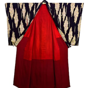 Könnte beinhalten: Ein traditioneller japanischer Kimono mit dunkelblauem Außenmaterial und einem sich wiederholenden Muster aus weißen und goldenen Rauten. Das Innenfutter ist leuchtend rot und bildet einen auffälligen Kontrast. Der Kimono wird offen präsentiert und zeigt sein volles Design.