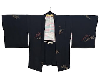 May include: A black Japanese kimono with a floral pattern. The kimono has a white lining with pink and blue stripes.