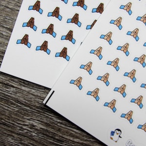 May include: Two sheets of stickers with a repeated image of two hands clasped together in prayer. The hands are brown with blue sleeves. The stickers are on a white background.