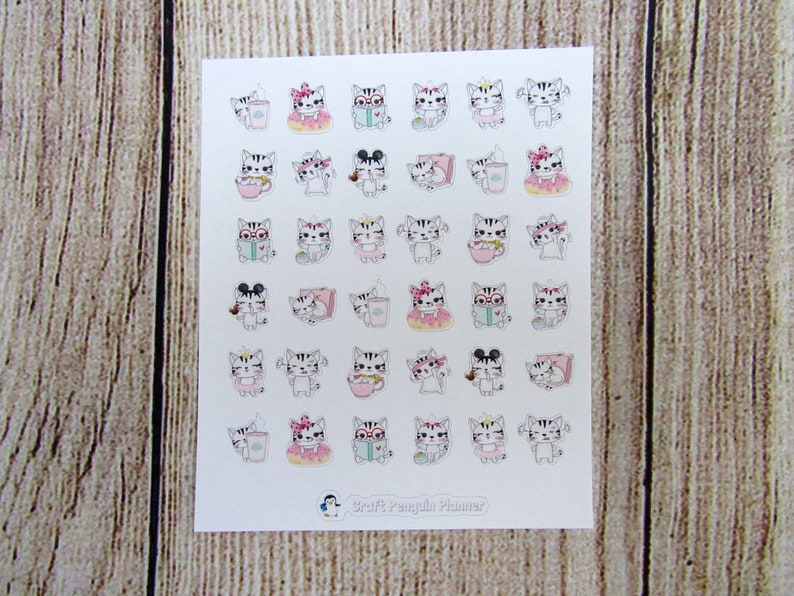 May include: A sheet of 36 cat-themed stickers featuring various activities like reading, drinking coffee, and wearing a crown. The stickers are white with pink and blue accents. The sheet is labeled "Scribble Penguin Planner".