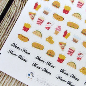 May include: A sheet of colorful stickers featuring various food items, including pizza, tacos, hot dogs, french fries, ice cream cones, and soda. The stickers have a cartoonish style with smiling faces. The text "Nom-Nom" is repeated multiple times on the sheet.