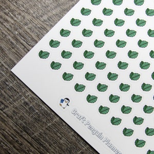 May include: A sheet of white sticker paper with a repeating pattern of green leaf stickers. The stickers are arranged in rows and columns. The text "Craft Penguin Planner" is printed in the bottom right corner of the sheet.