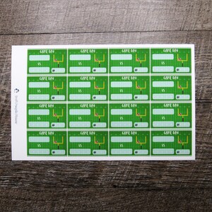 May include: A sheet of 16 printable football game day labels. Each label features a green field with a football goal post and a football. The text "GAME DAY" is at the top of each label with the word "VS" below it.