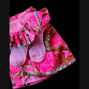 May include: Pink camouflage fabric with a ruffled edge and a pair of pink socks. The fabric has a white and brown pattern. The fabric has the word "EDGE" printed on it.