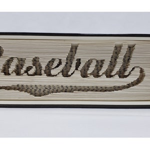 Könnte beinhalten: Eine Buchkunstskulptur des Wortes "Baseball" in einer kursiven Schrift. Das Buch ist in Schwarz gebunden und die Seiten sind gefaltet, um das Wort zu bilden.
