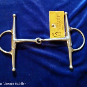 May include: A silver horse bit with a T-shaped mouthpiece and a D-ring on each side. The bit is labeled "Centaur Stainless Steel".