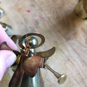 May include: A gold metal angel ornament with a halo and wings. The angel is holding a trumpet in its right hand.