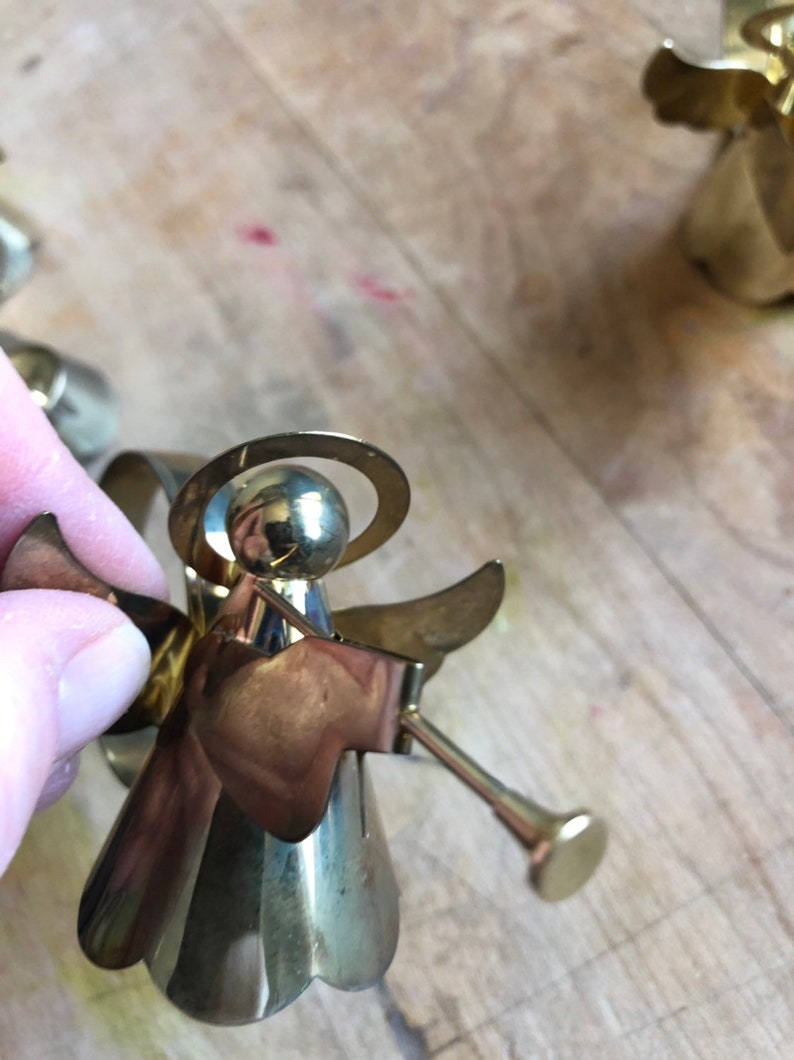 May include: A gold metal angel ornament with a halo and wings. The angel is holding a trumpet in its right hand.