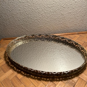 May include: A gold oval-shaped tray with a mirrored surface and a decorative, ornate border.