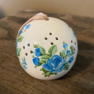 May include: White ceramic sphere with blue and green floral pattern and holes for scent to escape. The sphere has a string attached for hanging.